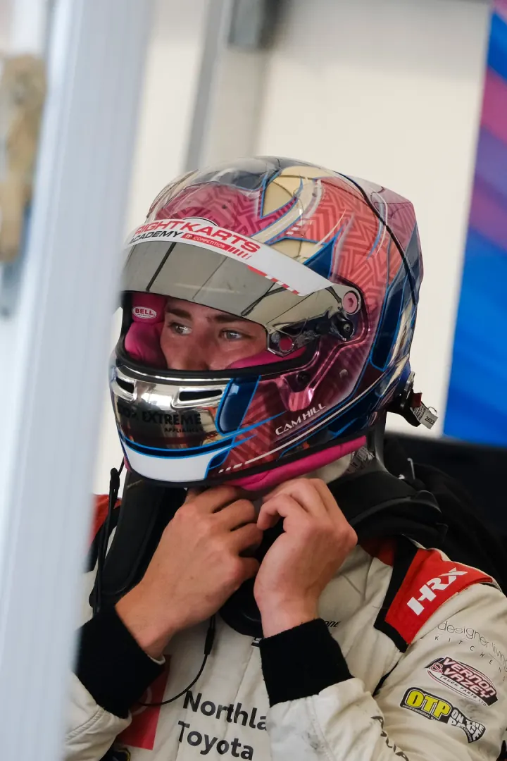 Cameron Hill in the paddock, visor up, adjusting his helmet strap.